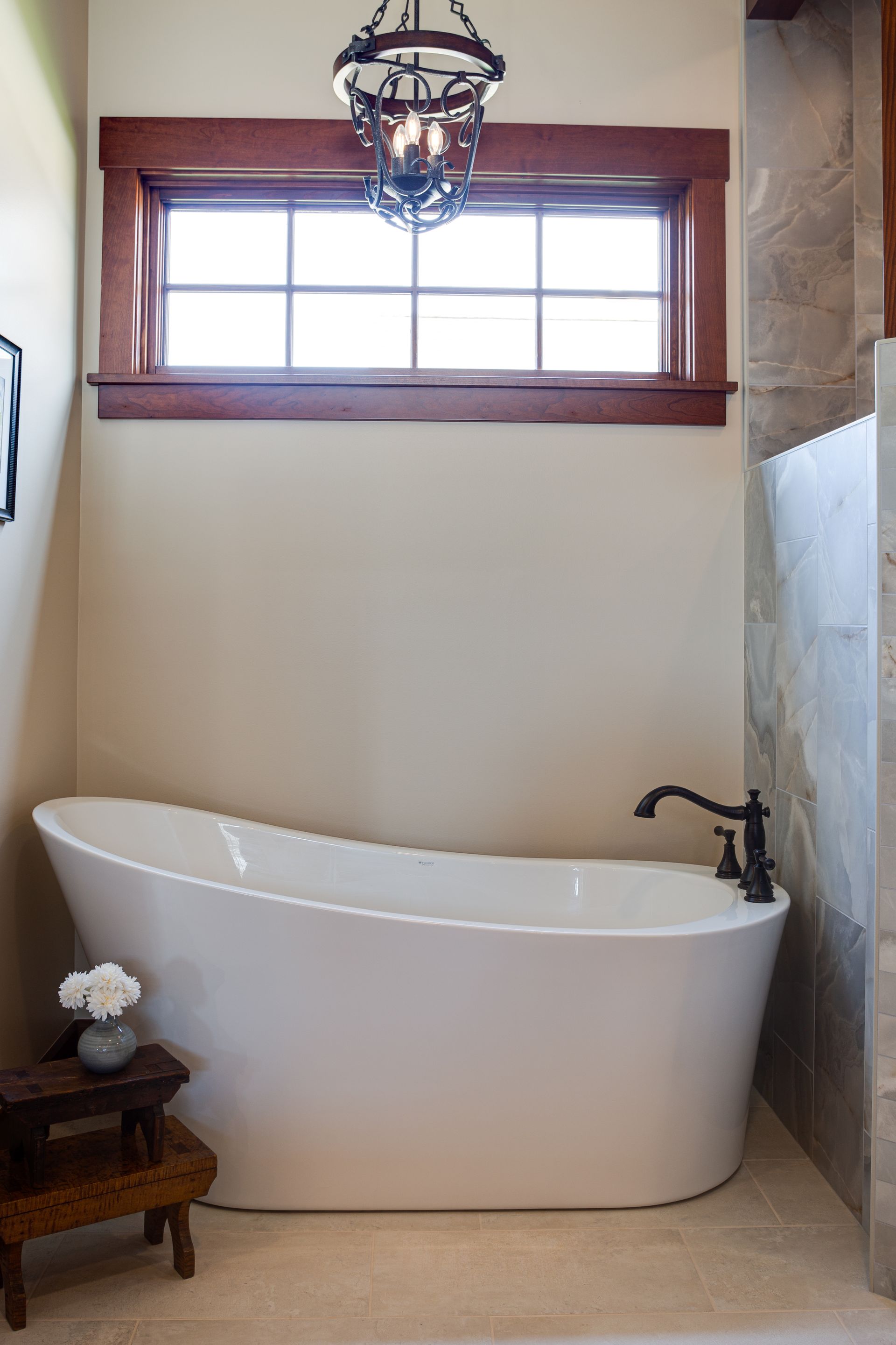 A bathroom with a tub under a window and a chandelier hanging from the ceiling.