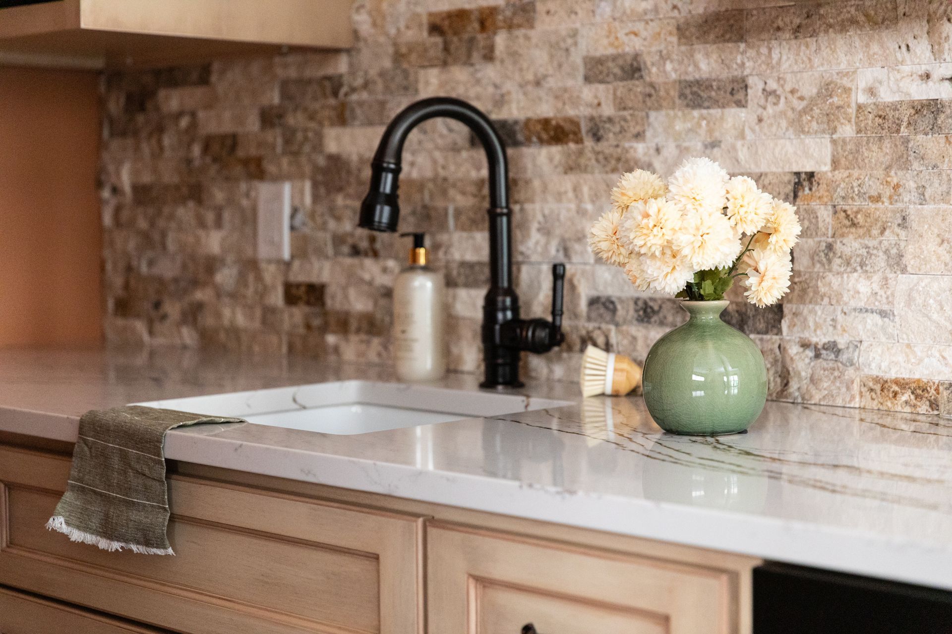 A kitchen sink with a vase of flowers on the counter.