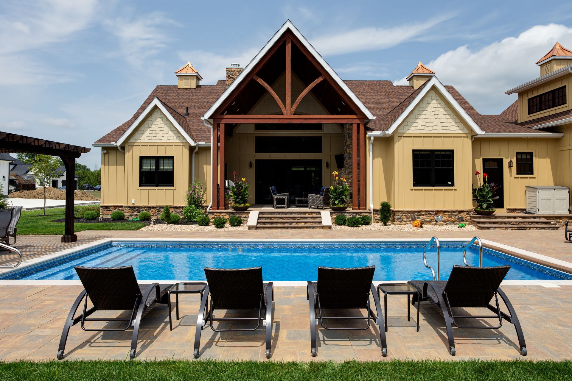 A large house with a large swimming pool in front of it and sun chairs.