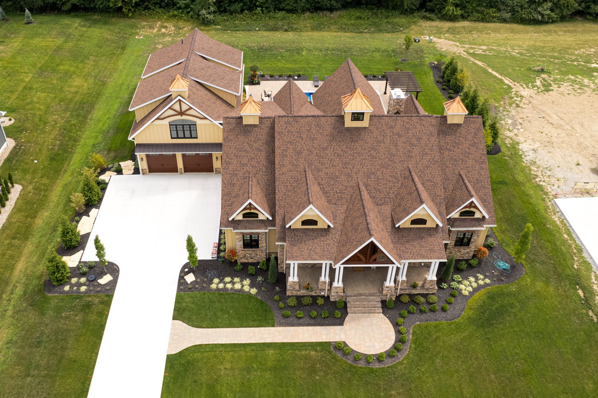 Aerial view of a large brown-roofed suburban house with a white driveway and front lawn