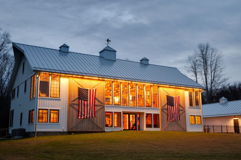 A large white barn house with American flags on the side of it.