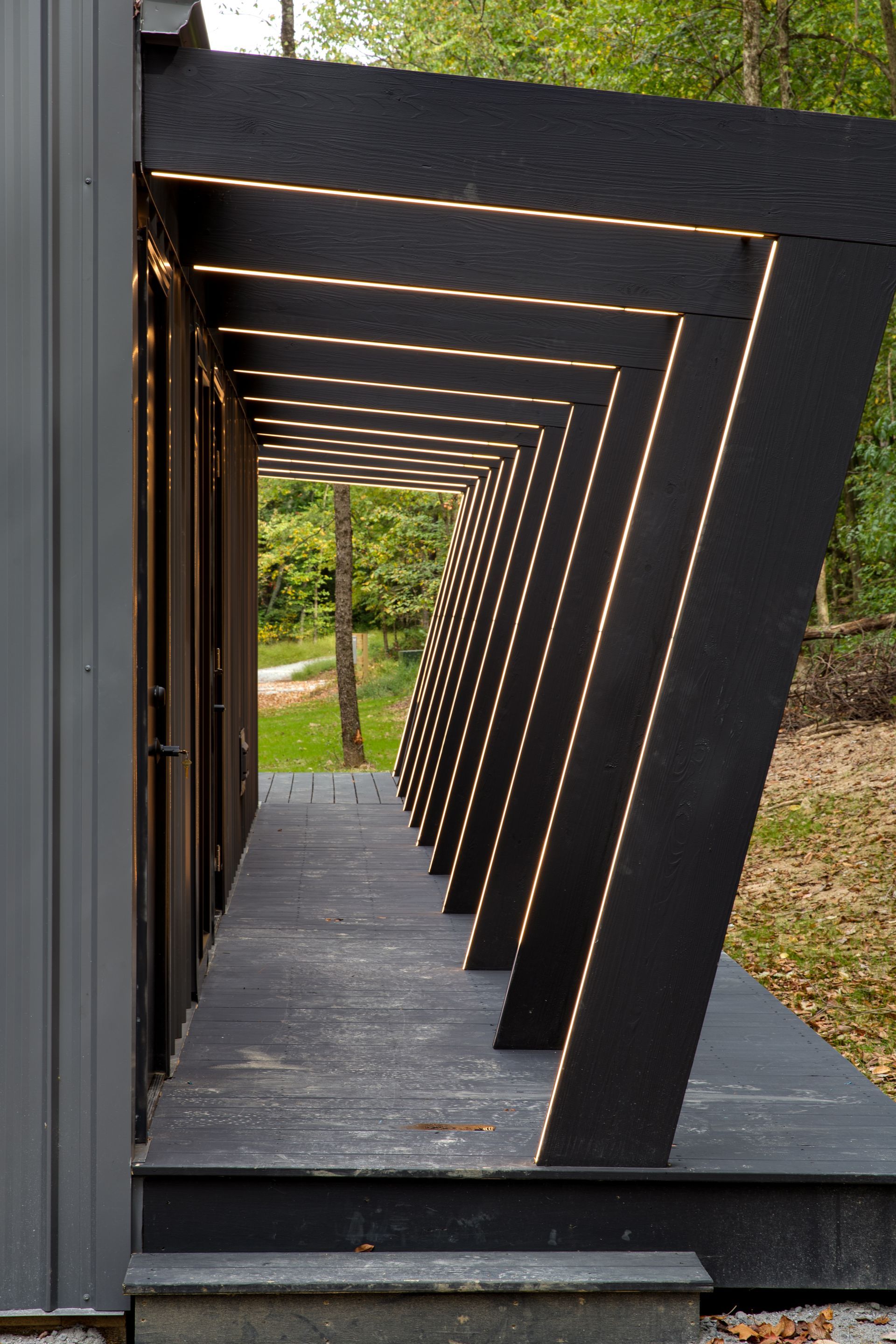 Black wooden walkway with repeating angled beams leading into a green outdoor area