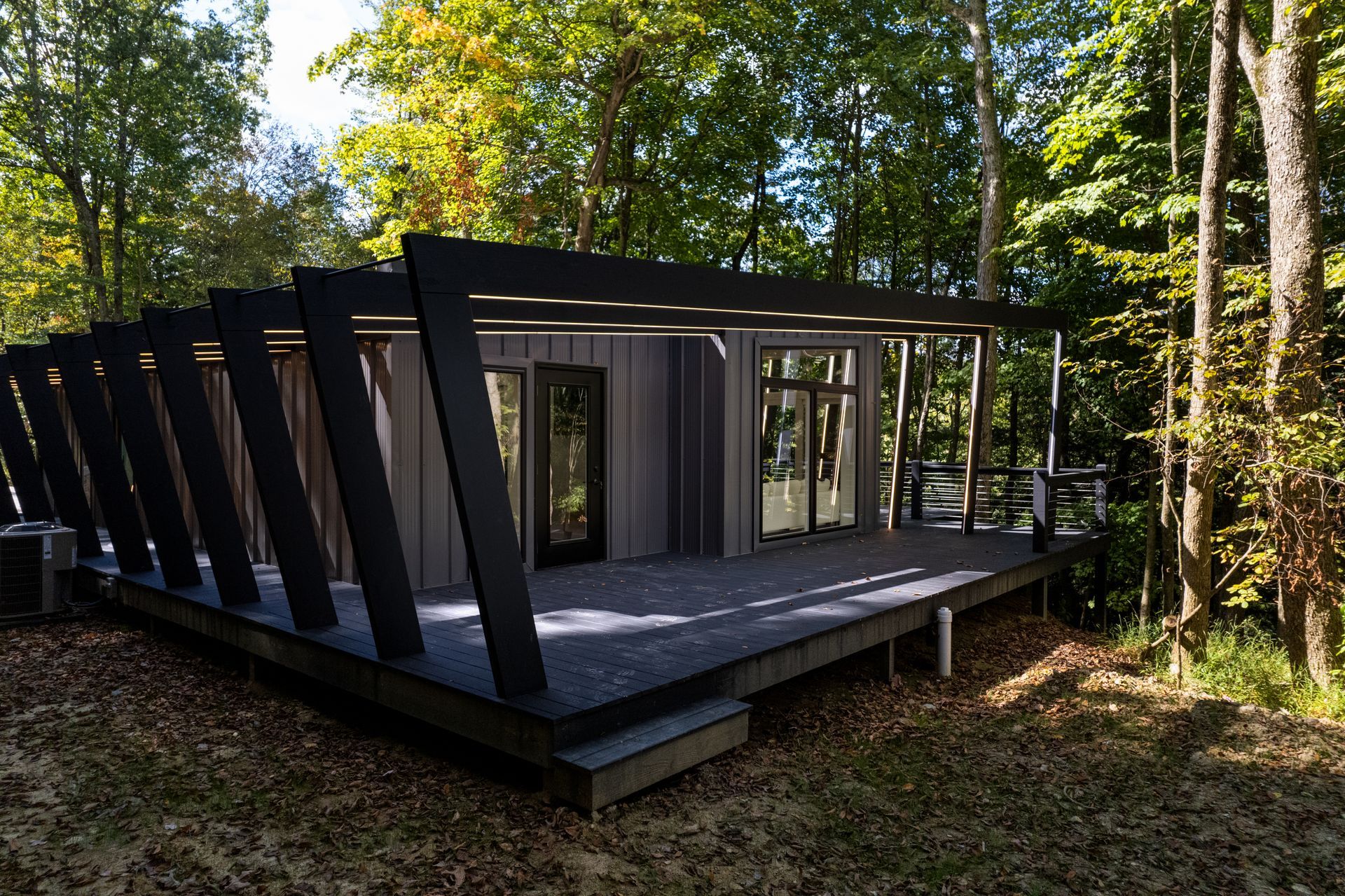 Modern black cabin with angular deck in a wooded forest clearing