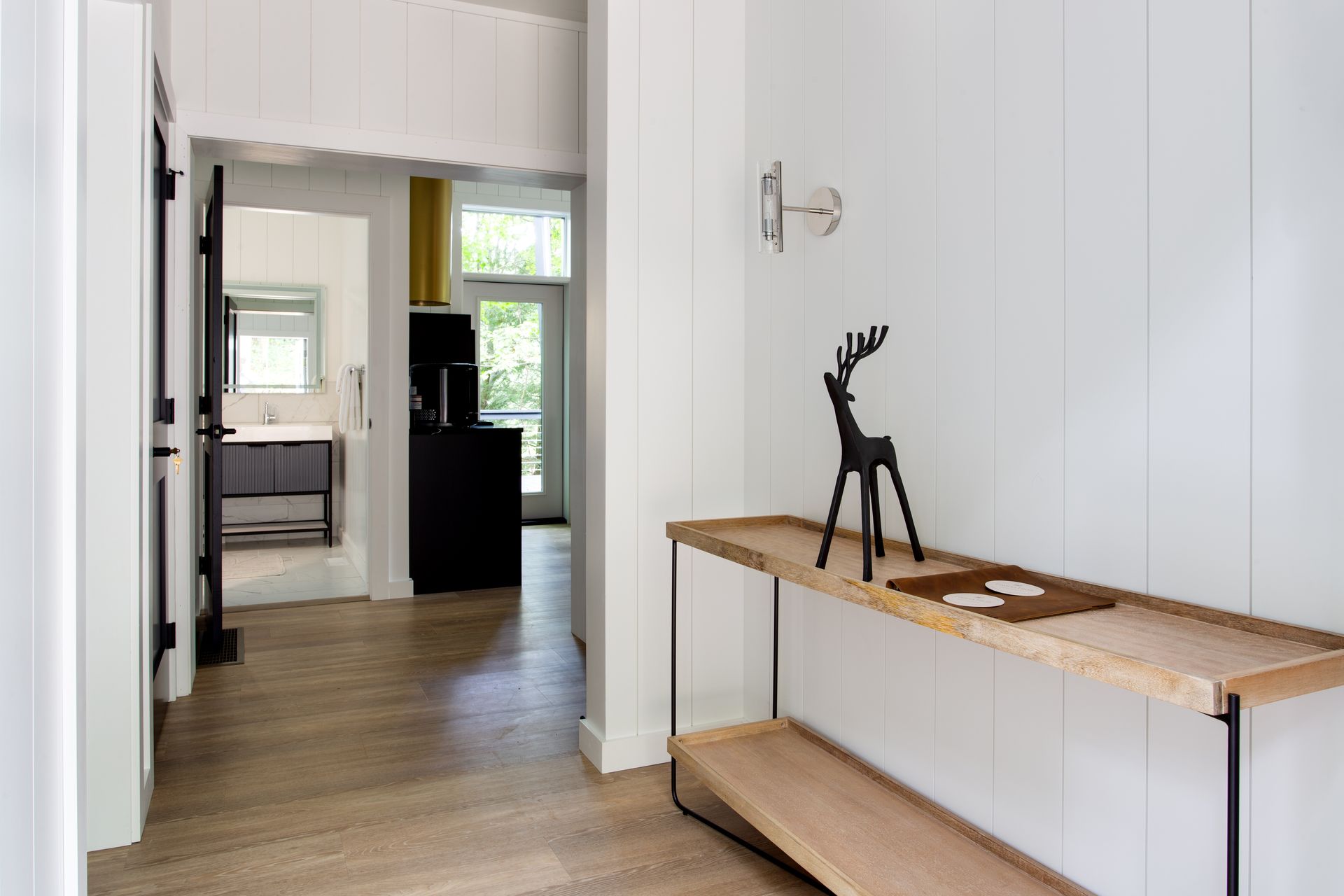 Bright hallway with white walls, wooden floor, and a wooden console table holding a small black deer sculpture.