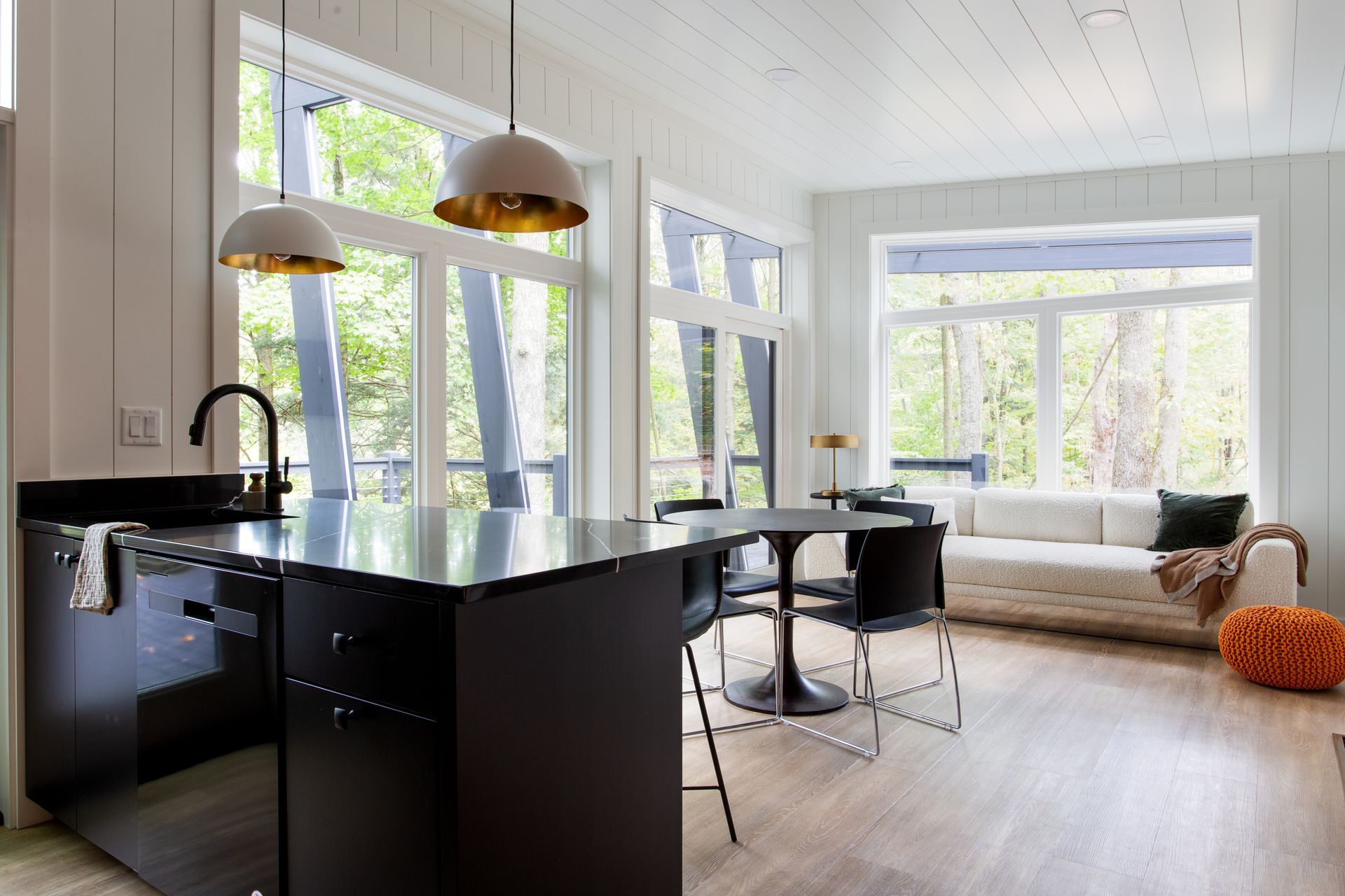 Modern open kitchen and bright living room with large windows, black island, and woven chair