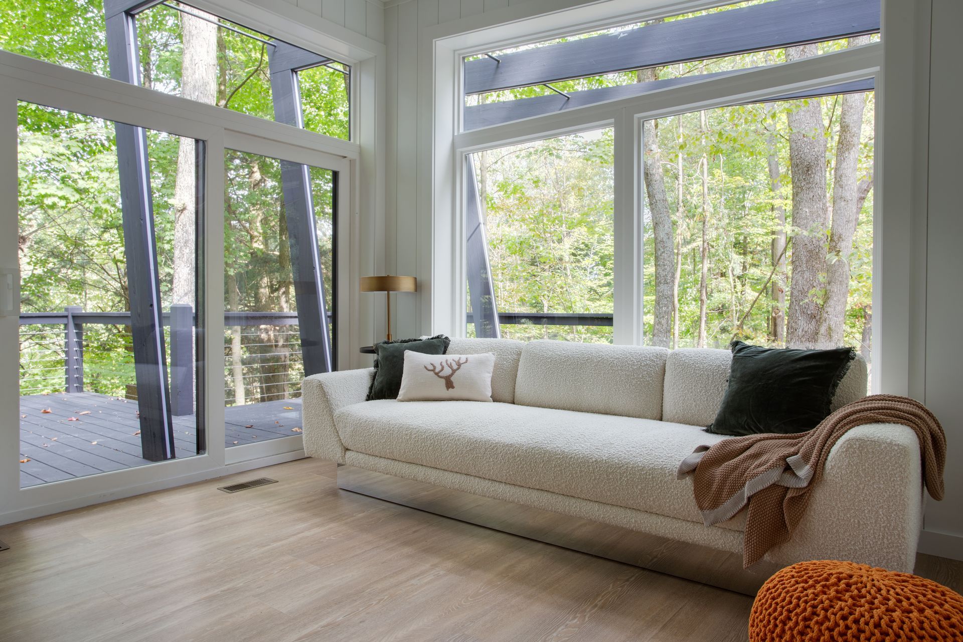 Bright modern living room with floor-to-ceiling windows, a white sofa, and a patterned throw blanket