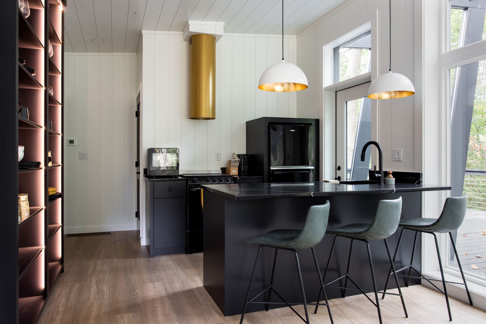 Modern kitchen with black island, gray stools, pendant lights, and large windows