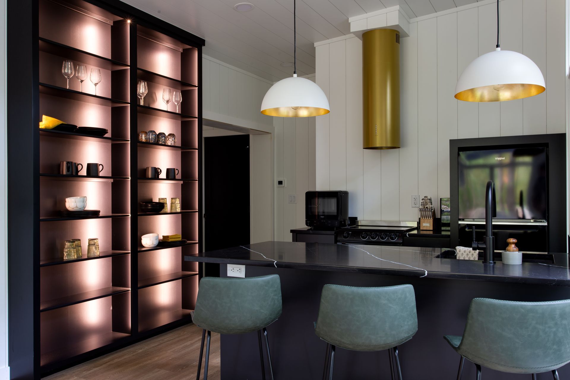 Modern kitchen with black island, teal stools, pendant lights, and illuminated shelving near dining area