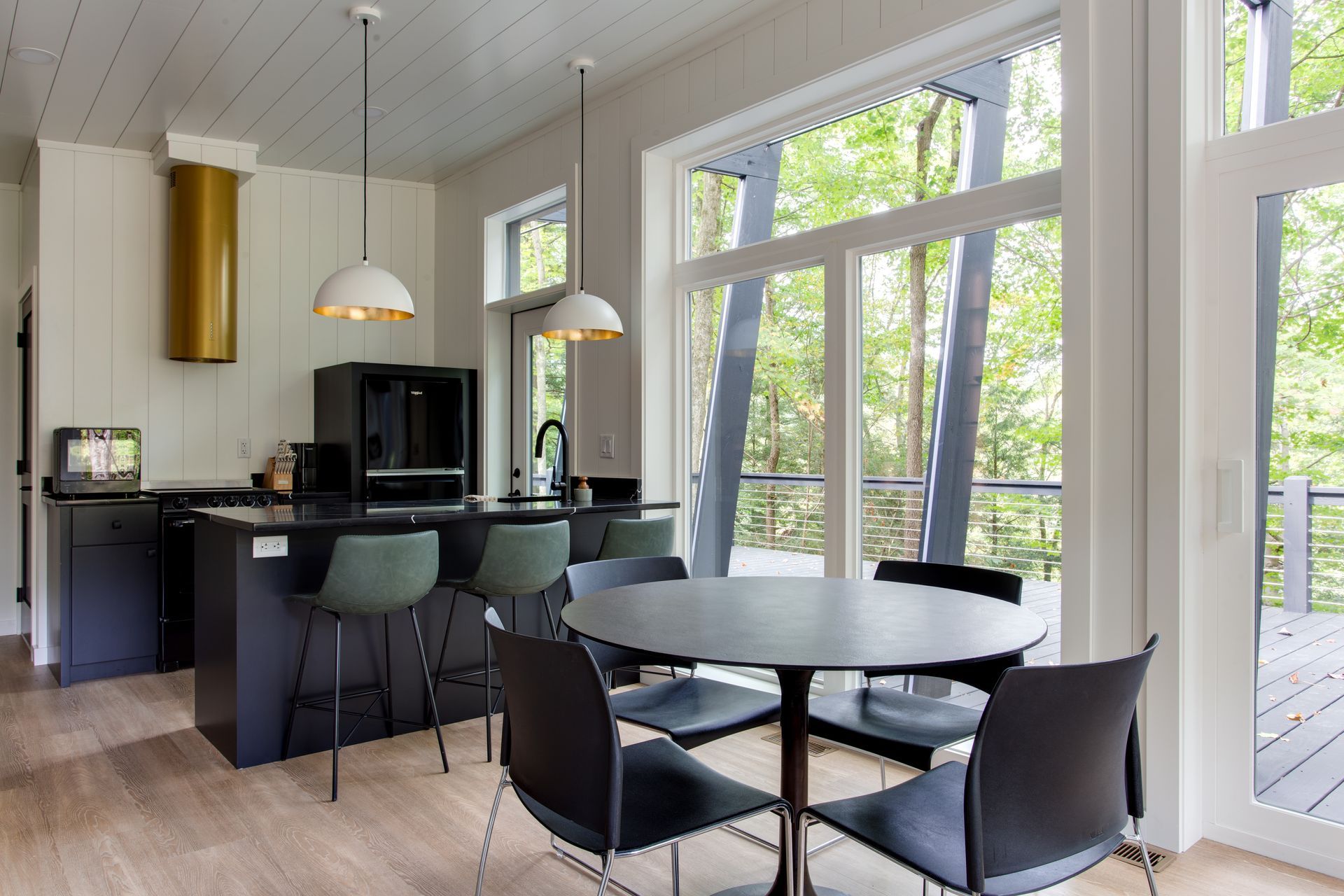 Bright modern kitchen-dining area with black chairs, round table, pendant lights, and large windows.