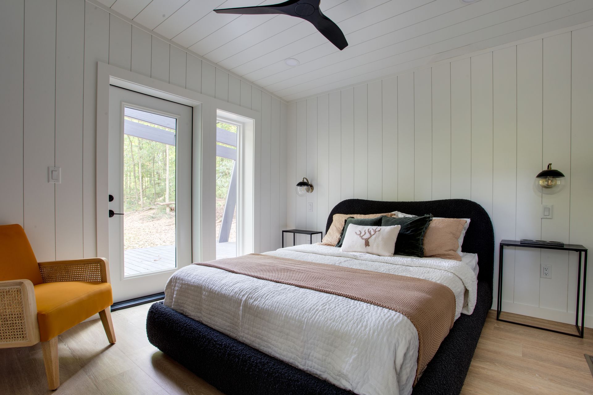 Bright modern bedroom with black bed, white walls, and French doors to the left