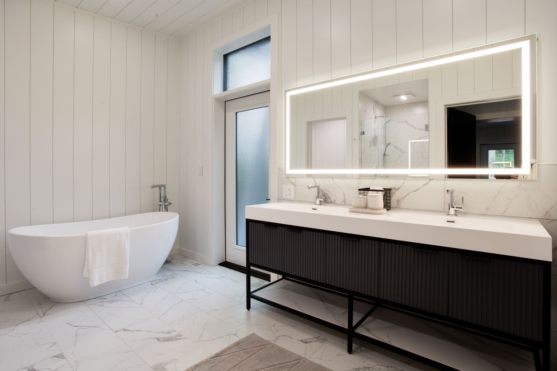 Modern bathroom with freestanding tub, long vanity, and illuminated mirror