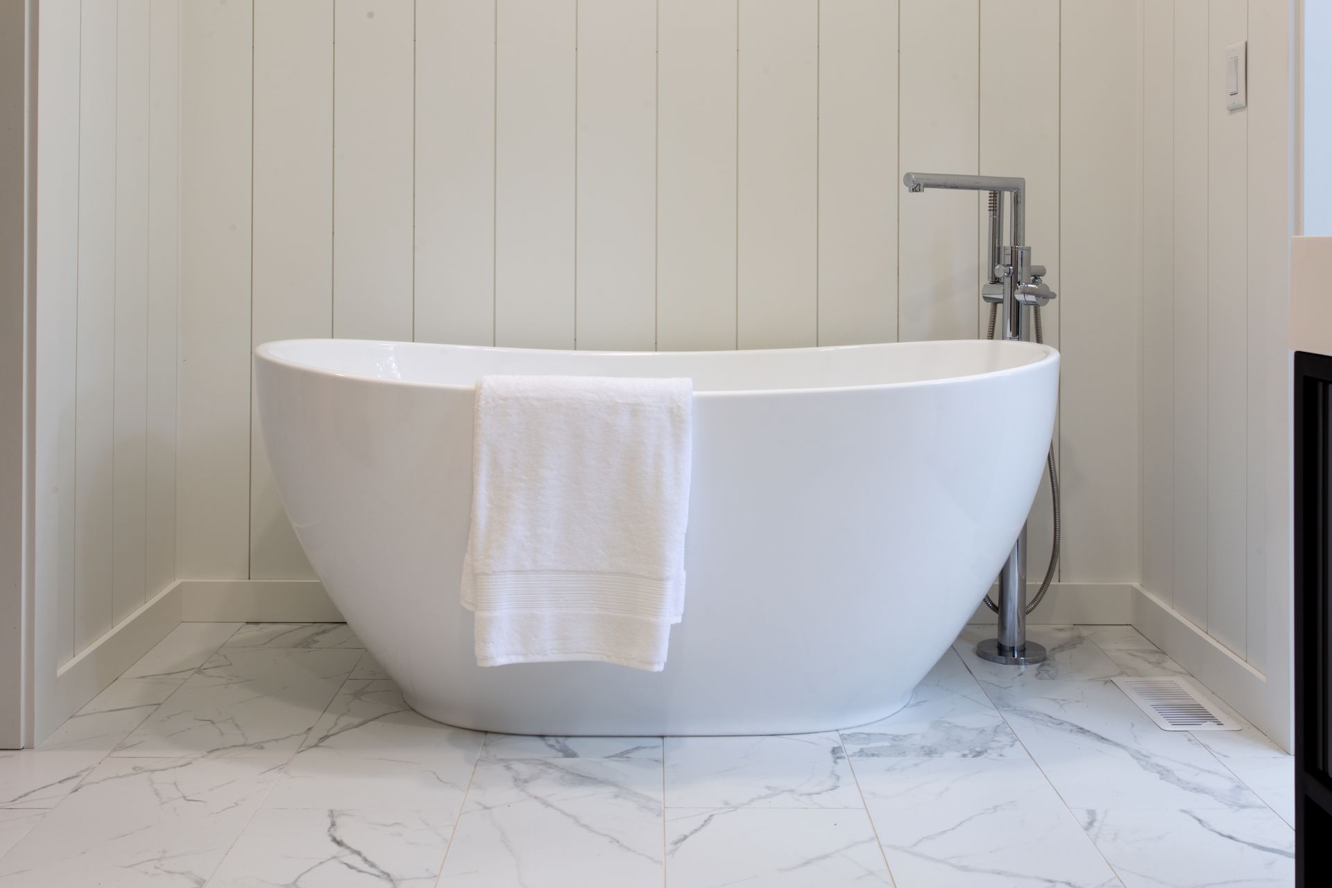 Freestanding white bathtub with towel in a bright, tiled bathroom