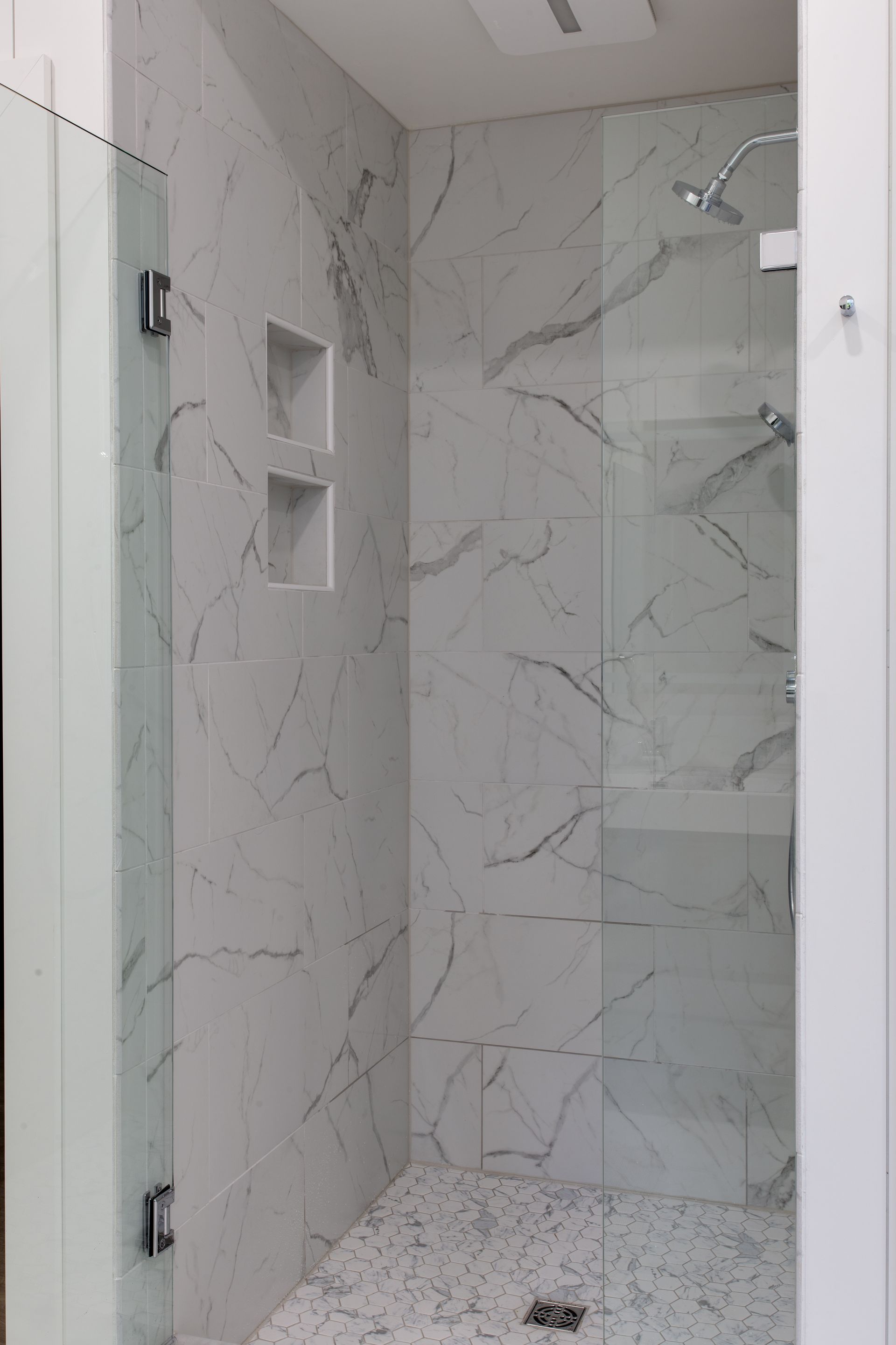 Small modern shower stall with white marble-look tile, built-in niches, and a wall-mounted showerhead.