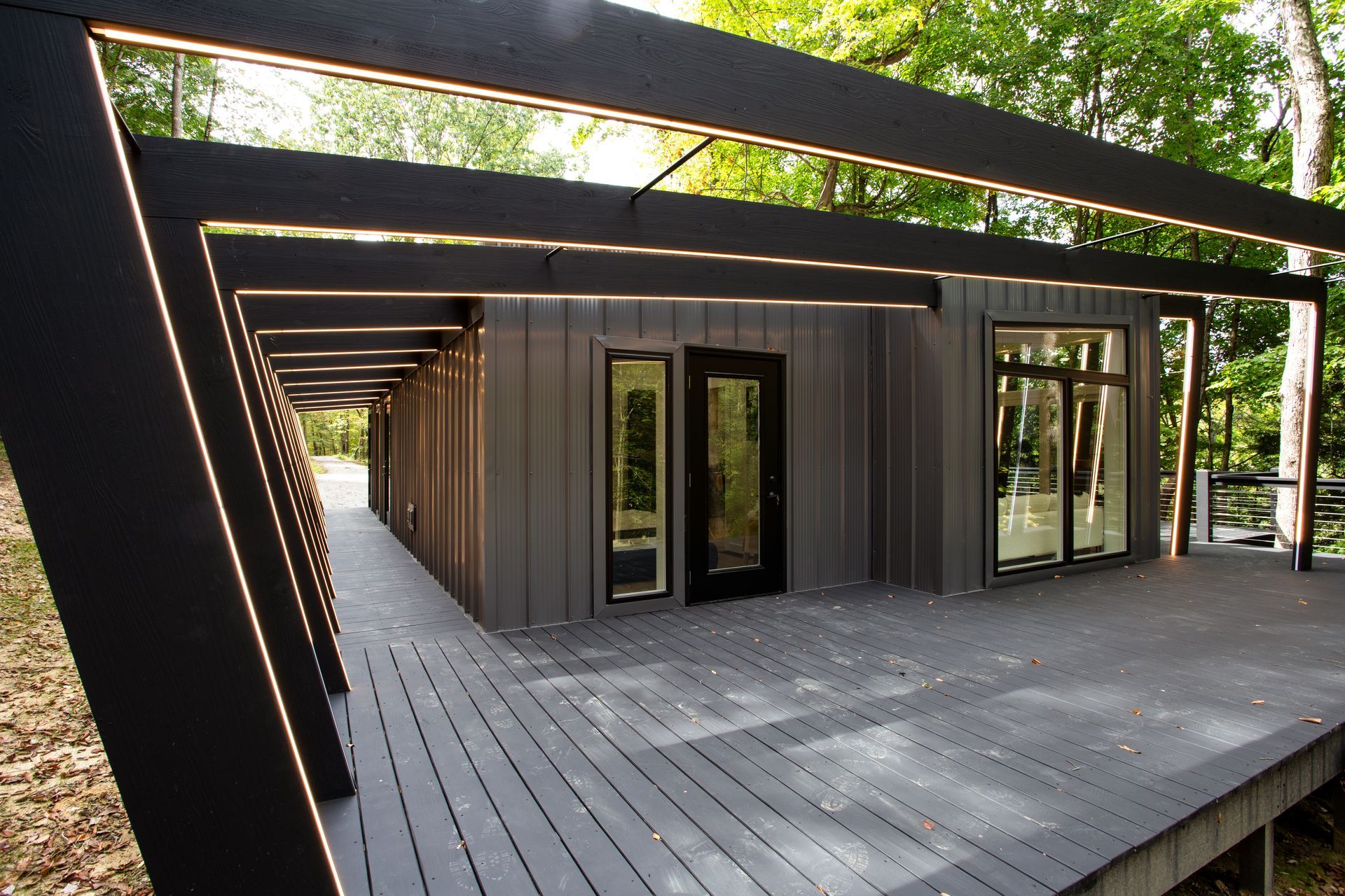 Modern dark metal house with a covered wooden deck and large windows in a wooded setting