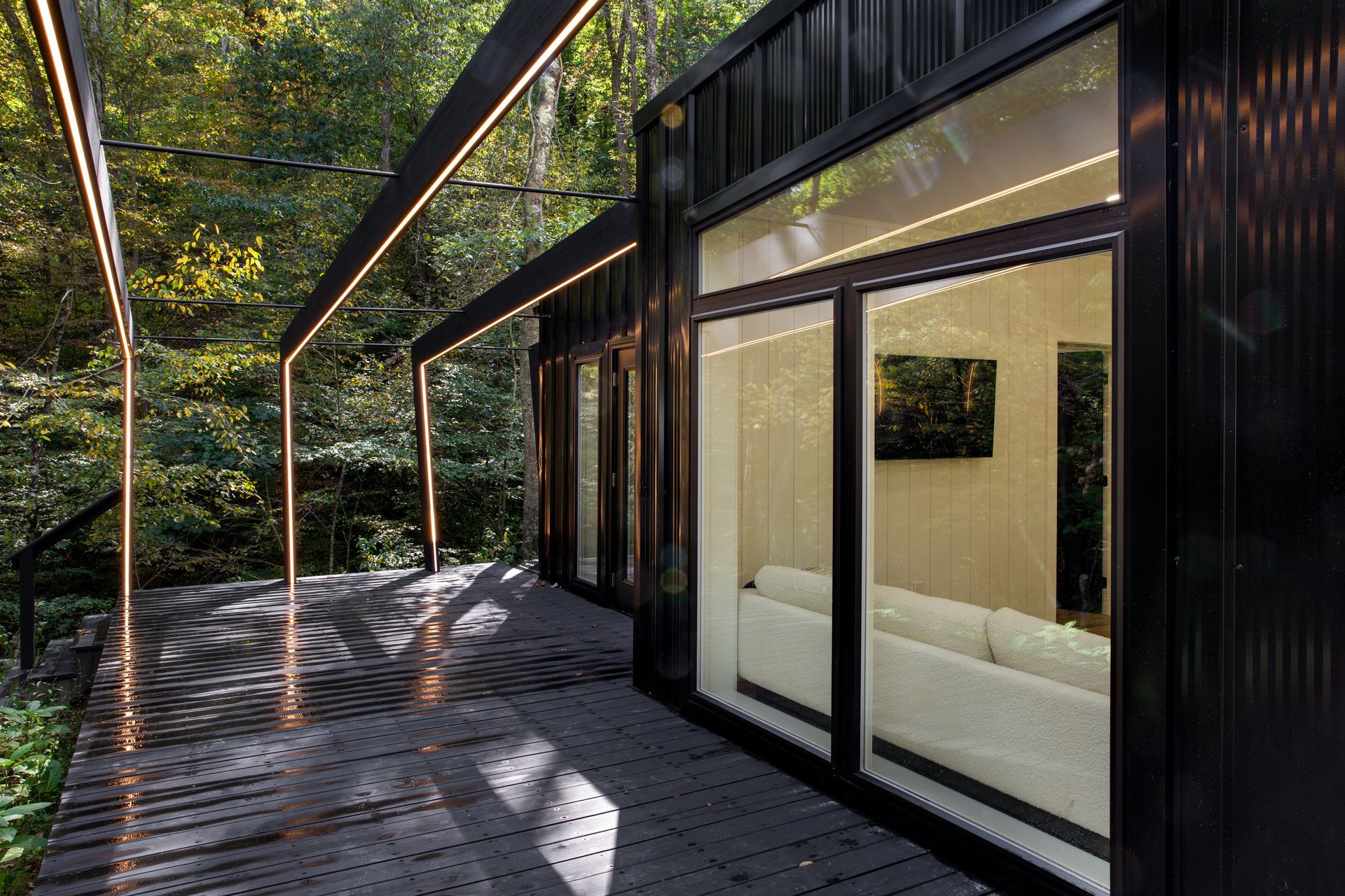 Modern black house with glass doors and a shaded deck beside trees
