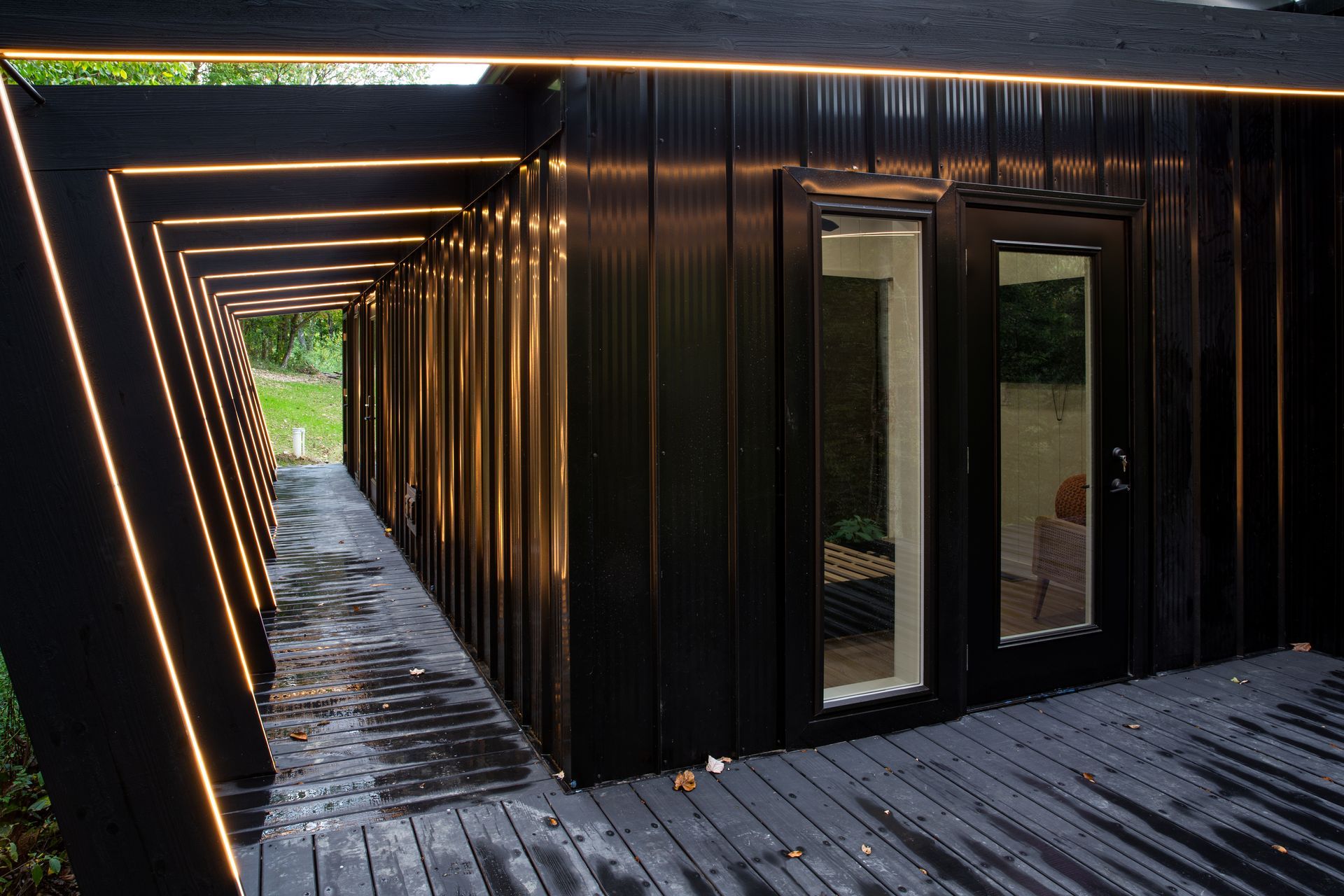 Modern black corridor with warm strip lights and glass doors beside a gravel path