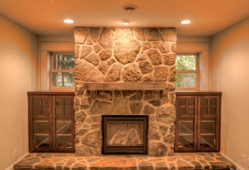 A living room with a stone fireplace and cabinets.