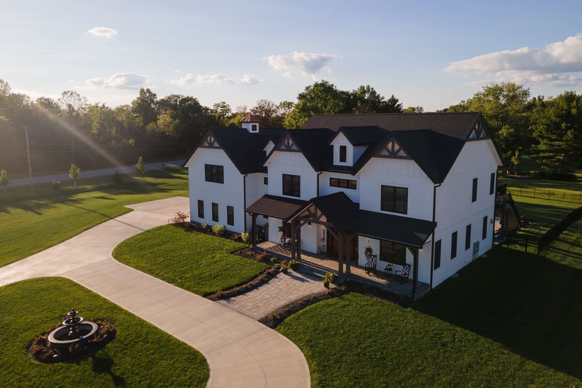 An aerial view of a large white house with a black roof surrounded by grass and trees.