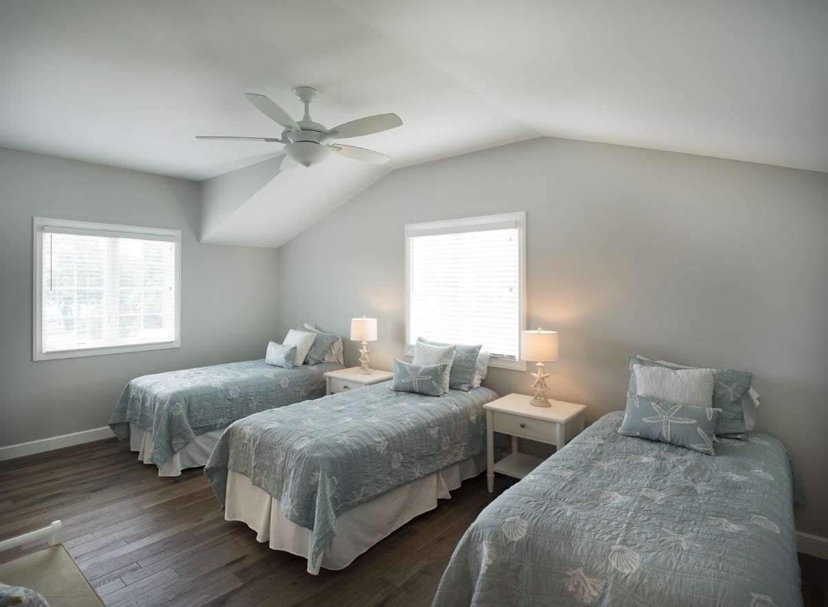 A bedroom with three beds and a ceiling fan.