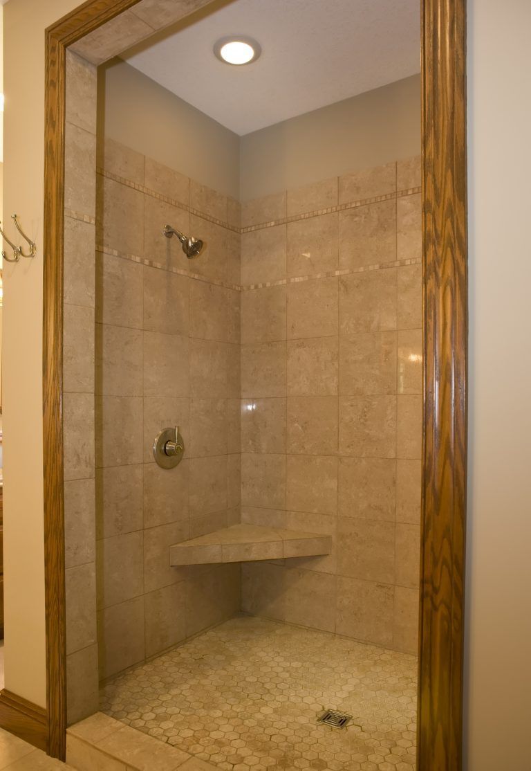 A bathroom with a walk in shower with a bench in the corner.