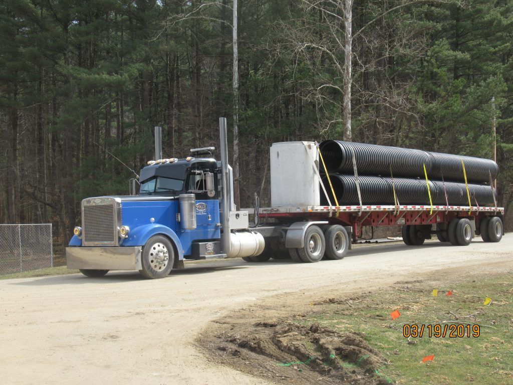 A blue semi truck is carrying a stack of black pipes