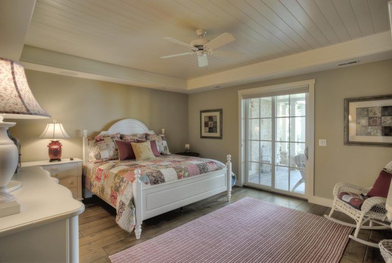 A bedroom with a large bed , a rocking chair , a rug and a ceiling fan.