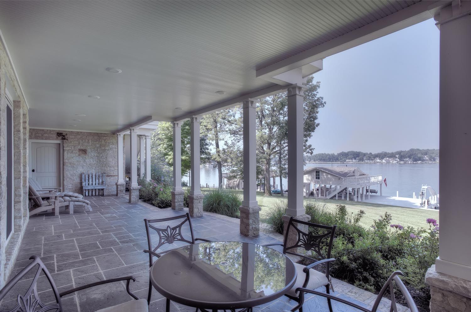 A porch with a table and chairs overlooking a lake.