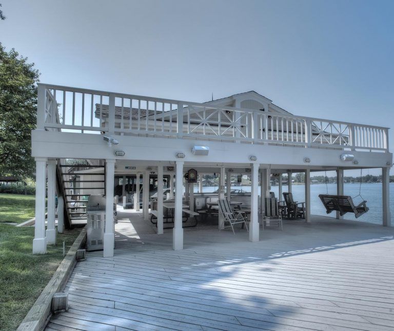 A white house with a large deck overlooking a body of water.