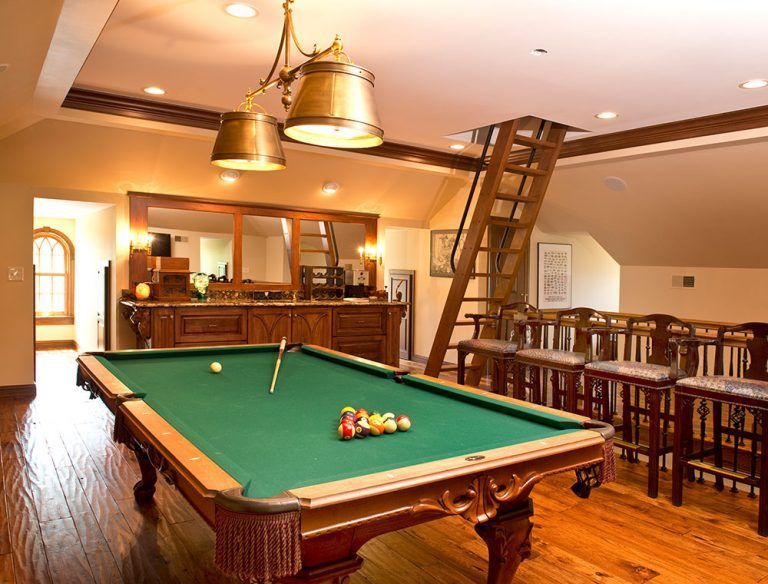 A pool table in a room with a bar and stairs.