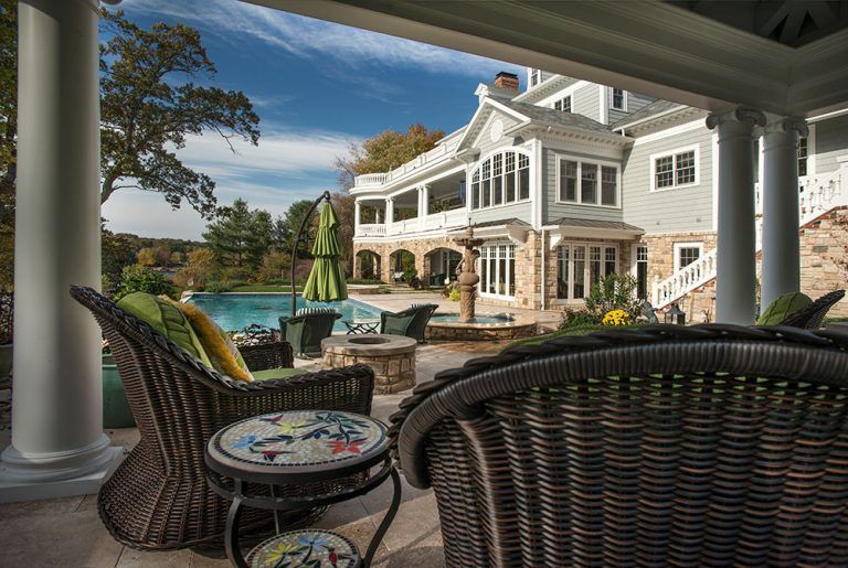 There is a large house in the background and a patio with chairs and a table.