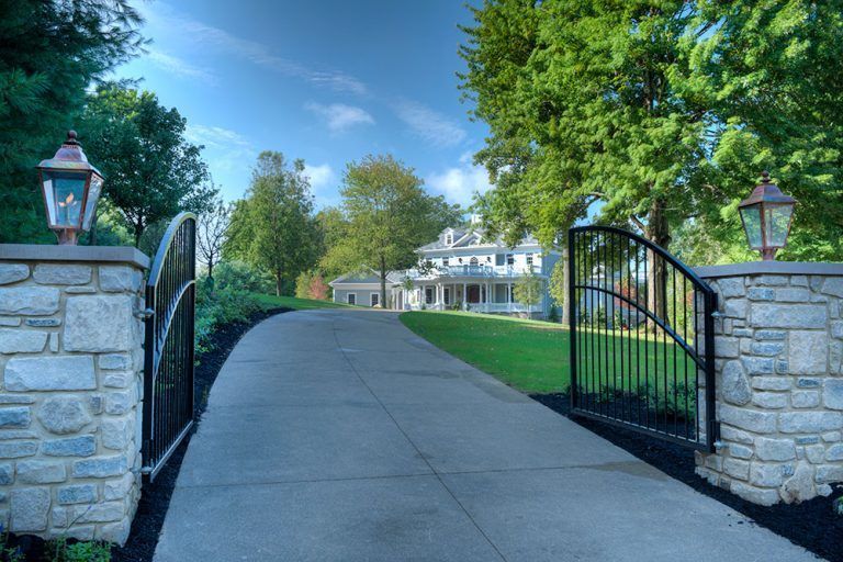 A driveway leading to a house with a stone wall and a gate.