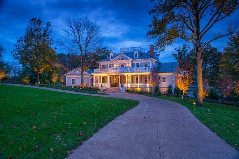 A large white house with a driveway leading to it is lit up at night.