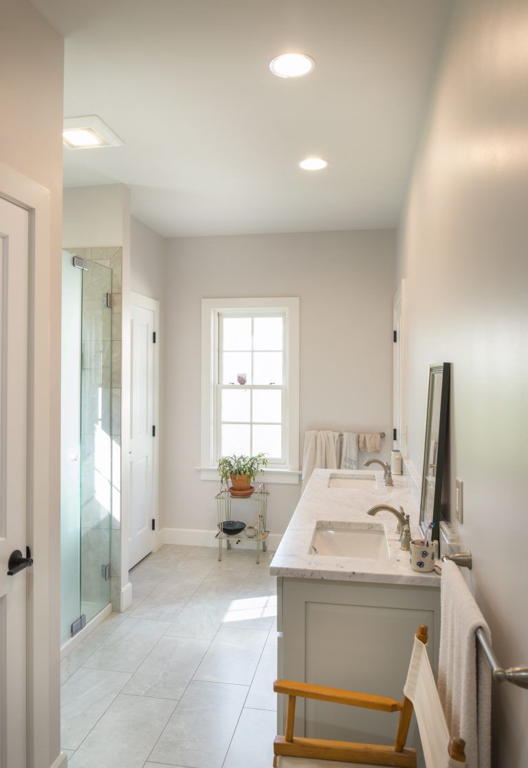 A bathroom with two sinks , a chair and a window.