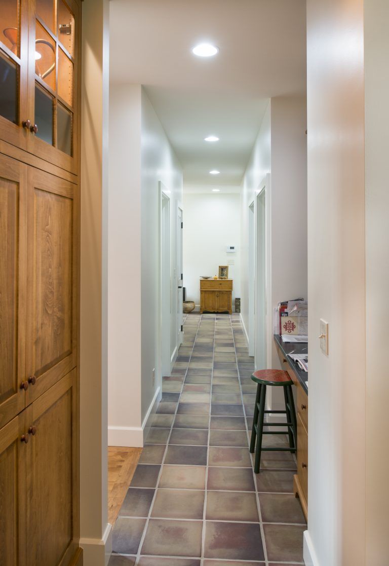 A long hallway with tile floors and wooden cabinets in a house.