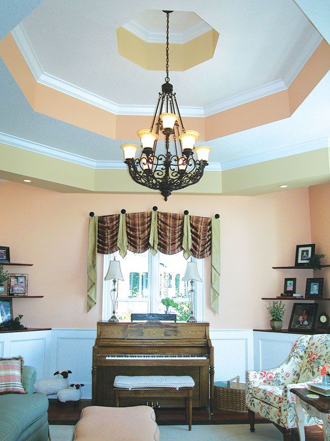 A living room with a piano and a chandelier hanging from the ceiling and a window.