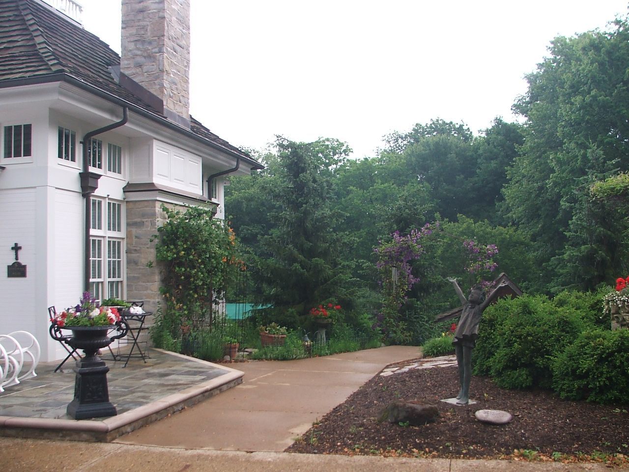 A white house with a chimney is surrounded by trees and bushes.