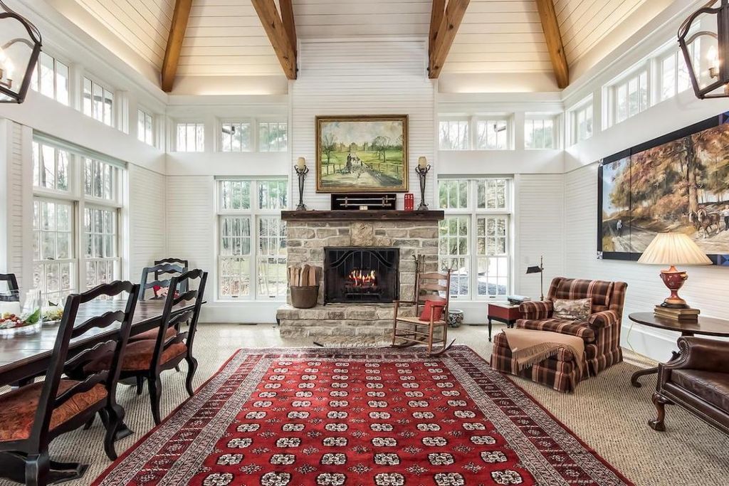 A living room with a fireplace , chairs , a table and a rug.