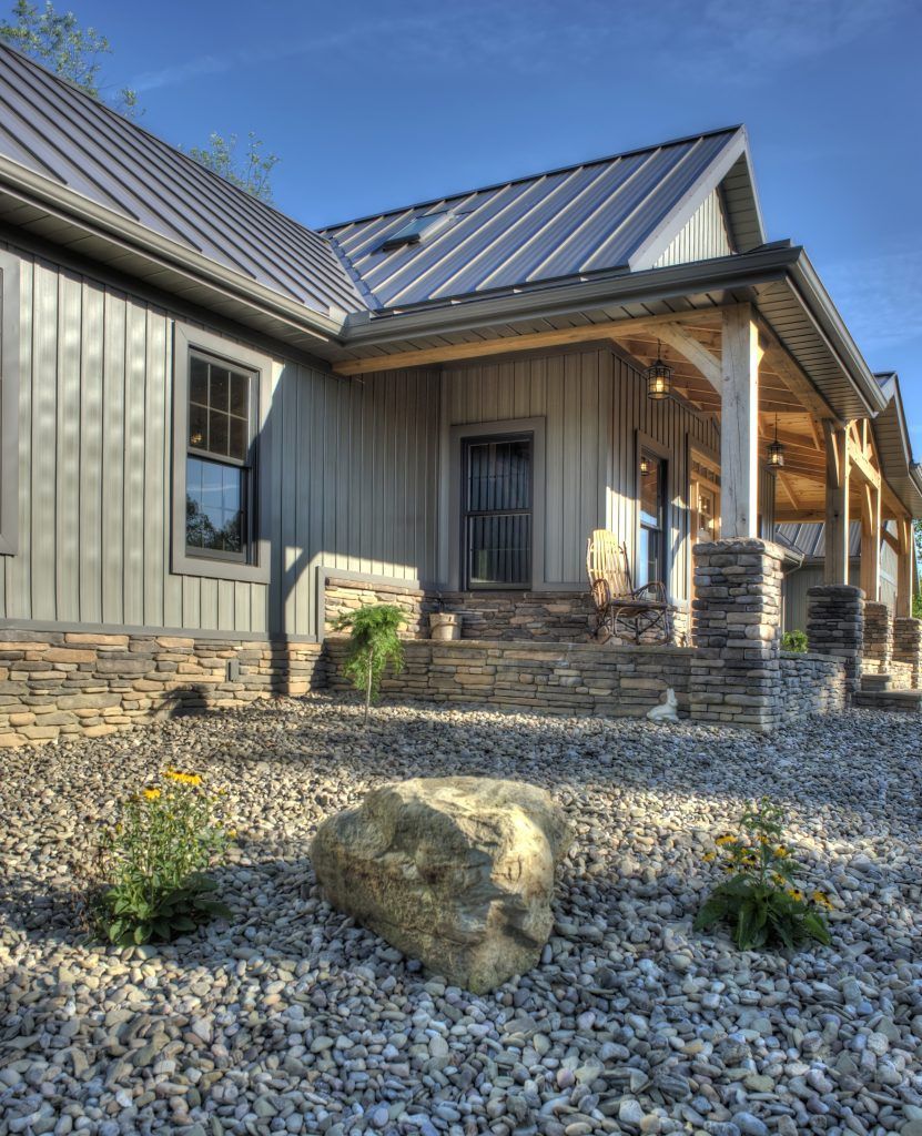 A house with a metal roof and a porch is surrounded by gravel.