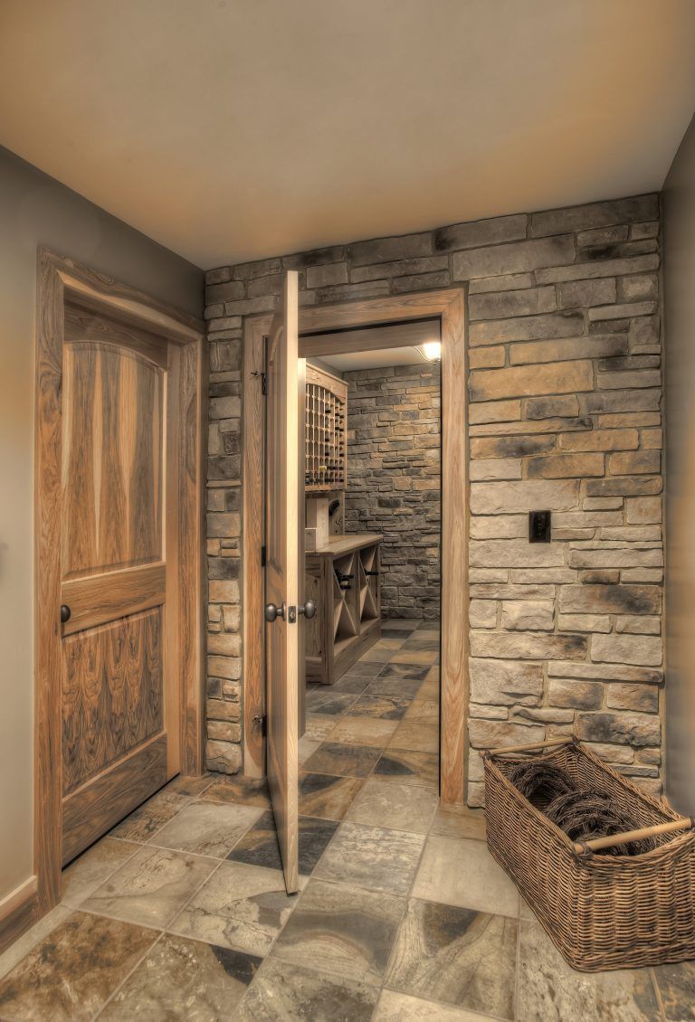 A hallway with a brick wall and a wooden door leading to a wine cellar.