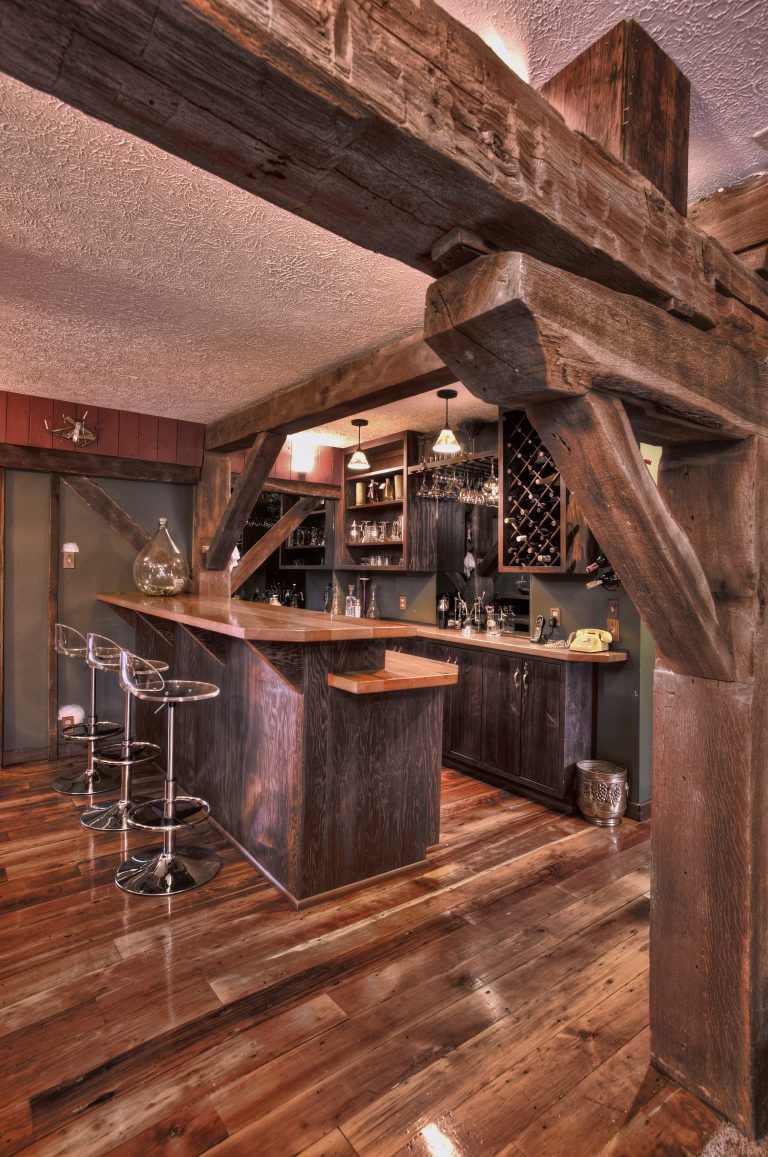A kitchen with hardwood floors, a bar, and stools and wooden beams