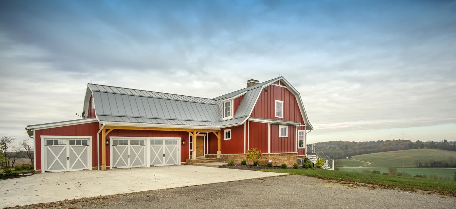 A large red barn is sitting on top of a hill with beautiful scenery in the background.