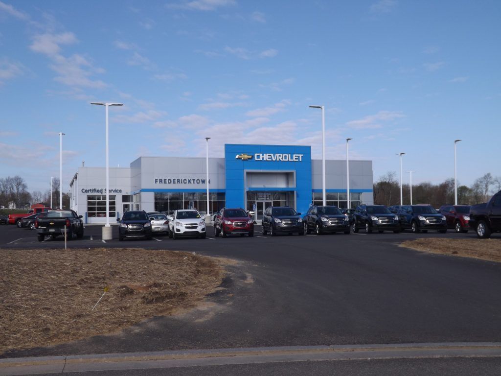 A row of cars are parked in front of a car dealership.