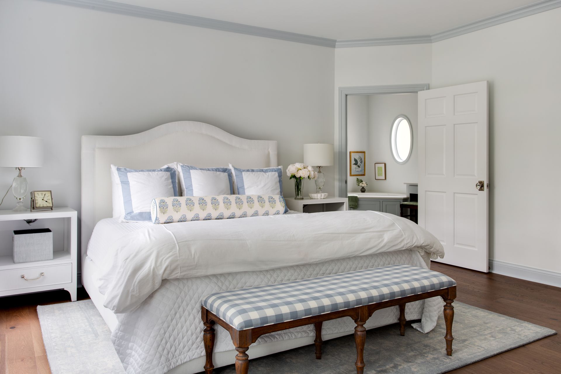 A bedroom with a bed , nightstands, a bench and a mirror.