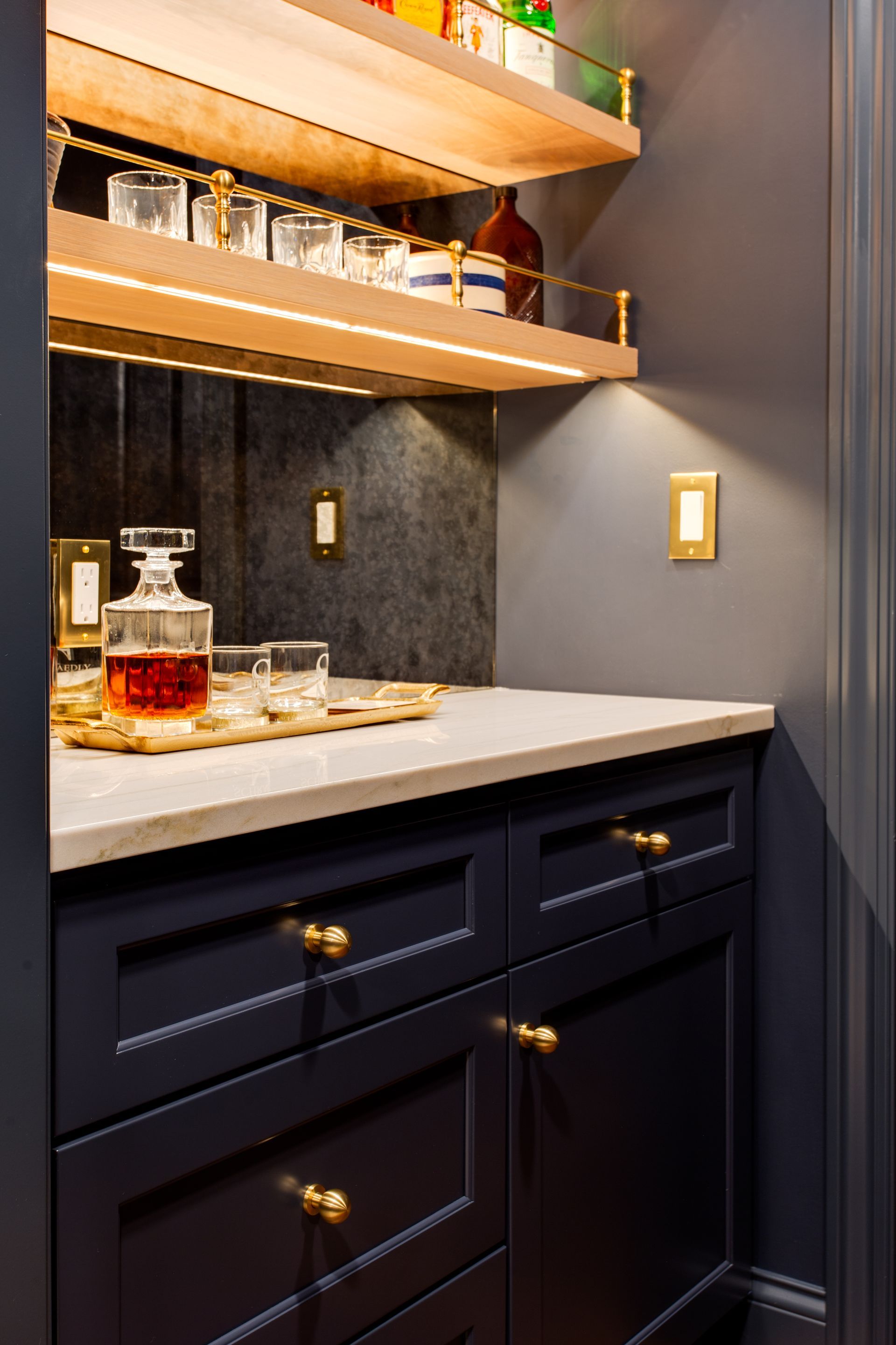 Stylish dark bar cabinet with marble countertop, glass shelves, and liquor bottles in a narrow nook.