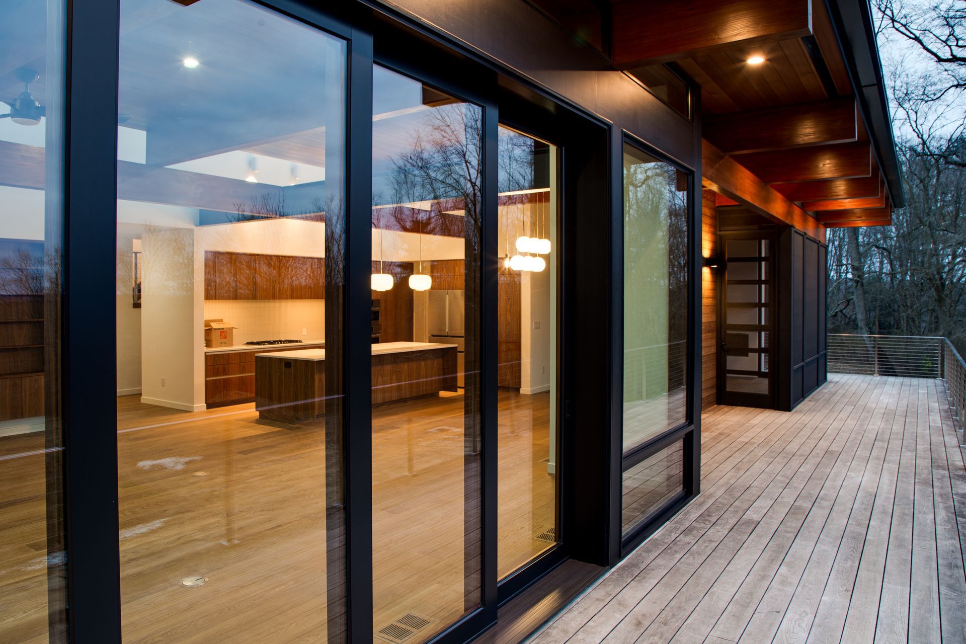 Modern house exterior with floor-to-ceiling glass windows and a wooden deck at dusk