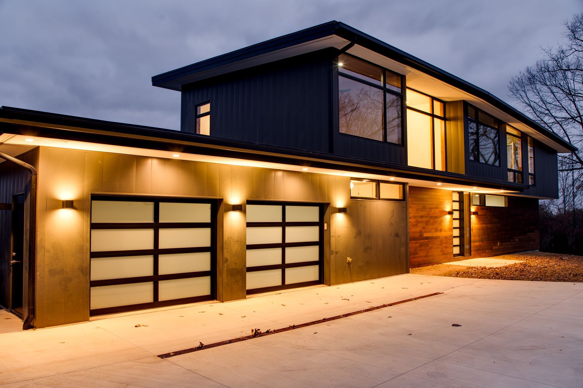 Modern two-story house with warm lights and a double garage at dusk
