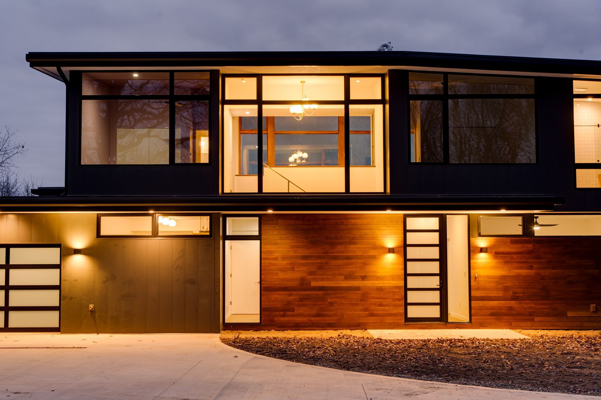 Modern two-story house exterior at dusk with warm interior lights and wood-paneled facade