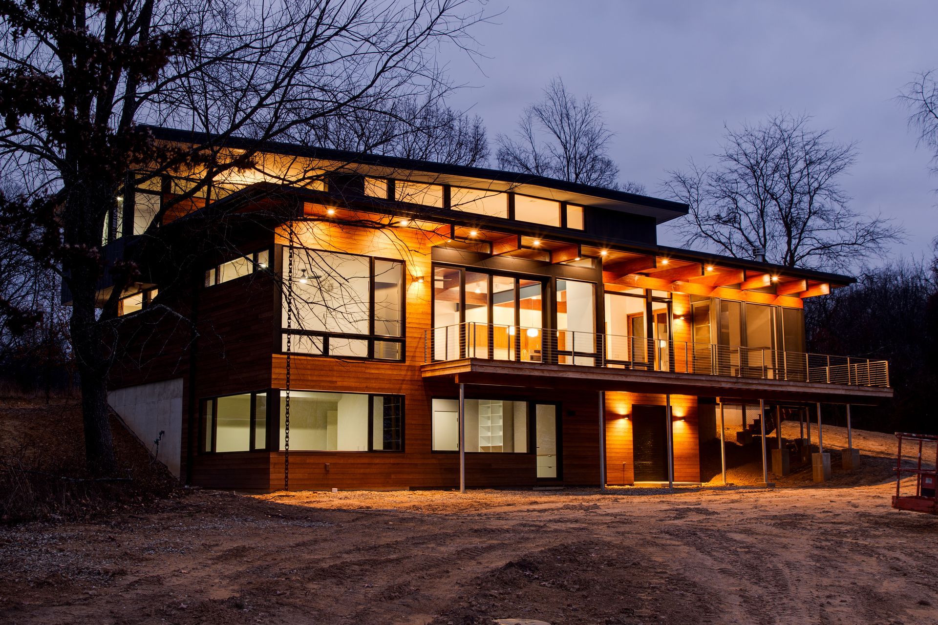 Modern two-story house with warm lights glowing at dusk in a wooded setting