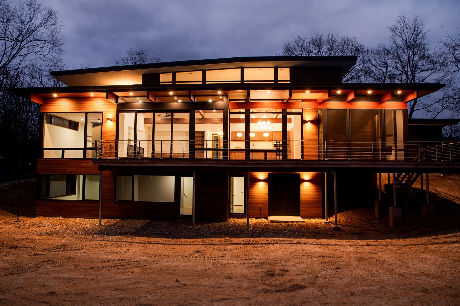 Modern house glowing warmly at dusk, with large windows and a dark exterior