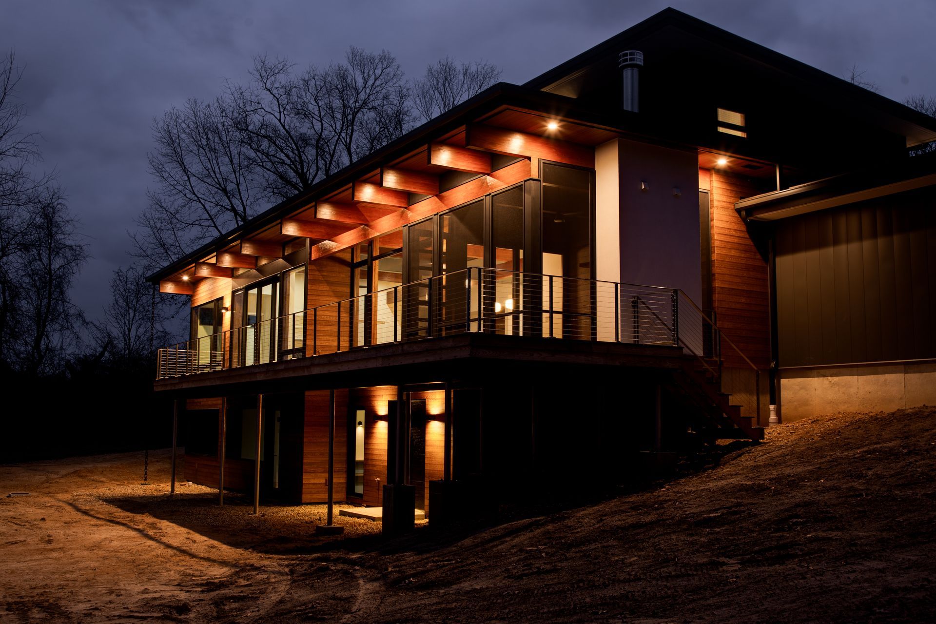Modern house with warm porch lights at dusk, set among trees on a hillside